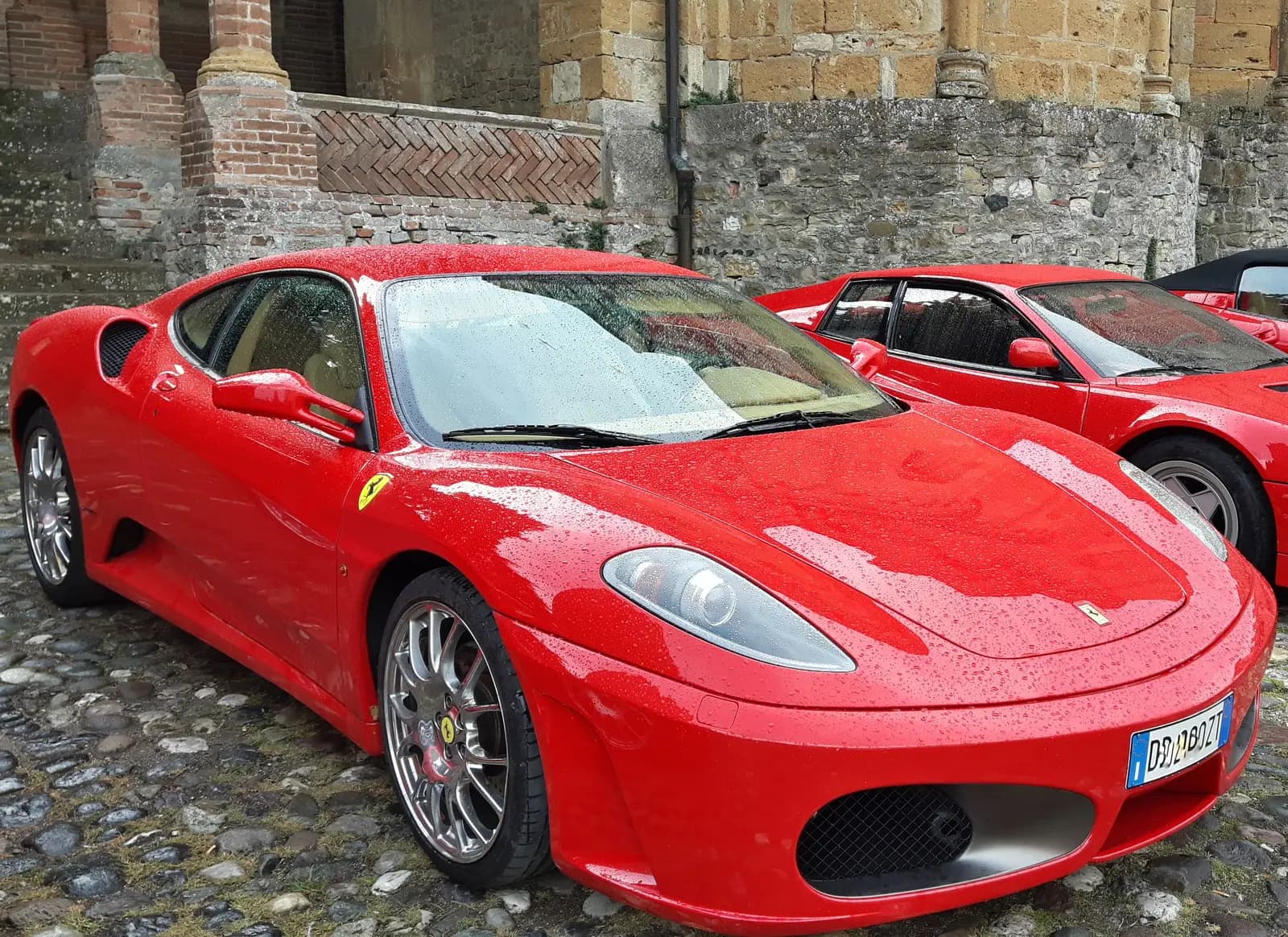 Red Ferraris parked on wet cobblestones in the rain